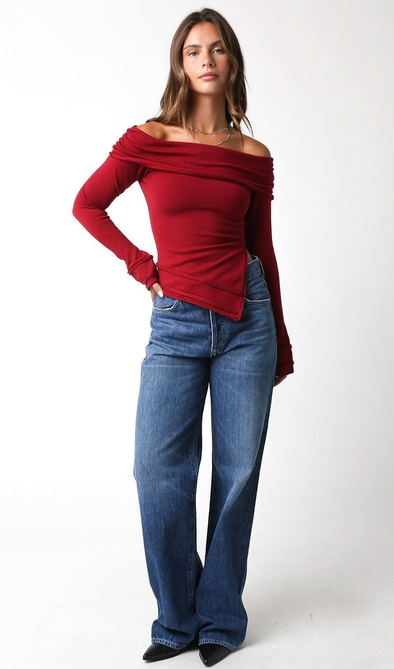Woman wearing a red off-shoulder top and blue jeans on a white background