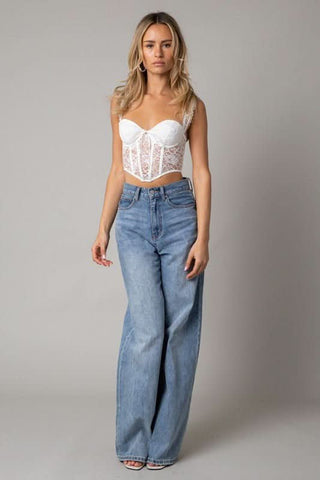 Model wearing a white lace corset top with high-waisted jeans