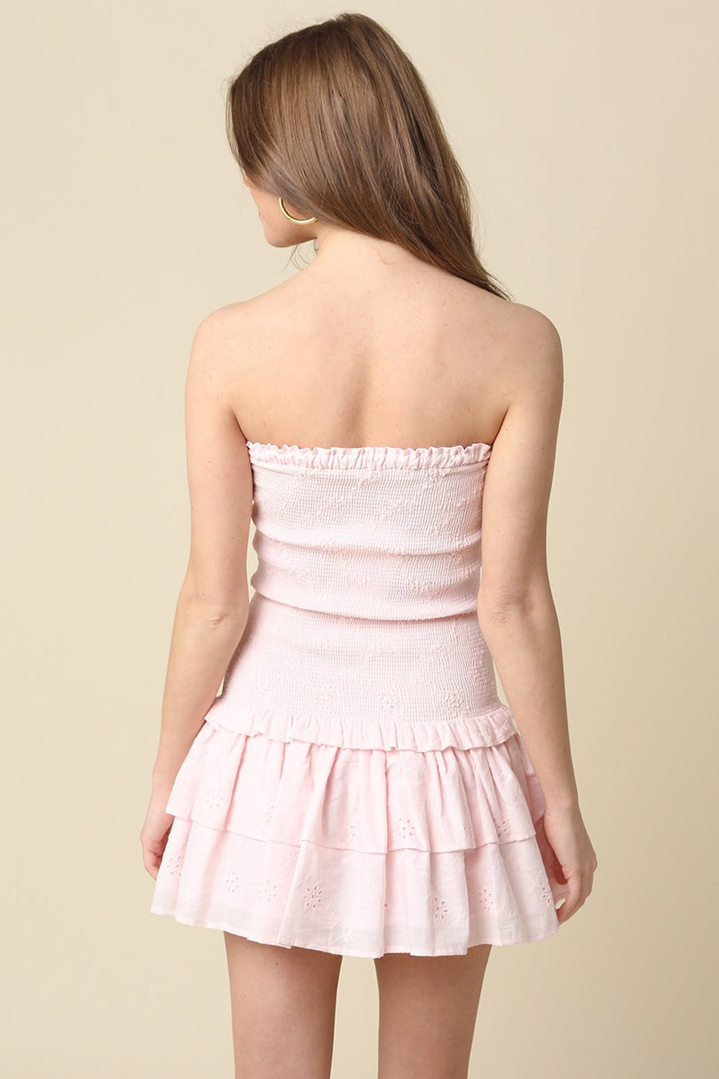 Back view of the light pink eyelet strapless mini dress showing the tiered ruffle skirt and smocked detail