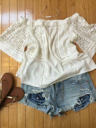 Flat lay of white off the shoulder top styled with distressed denim shorts