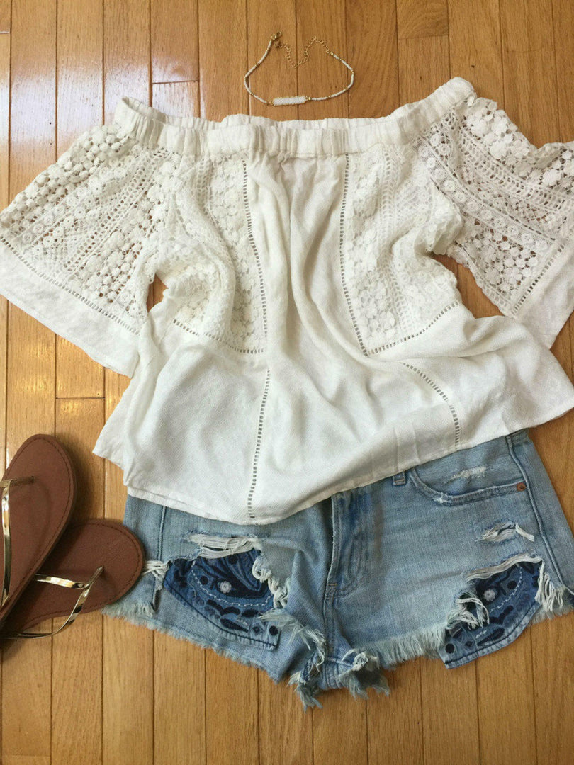 Flat lay of white off the shoulder top styled with distressed denim shorts