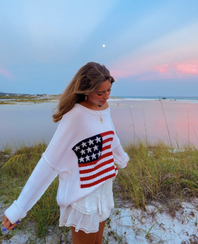 Woman wearing white American flag sweater off one shoulder with skirt
