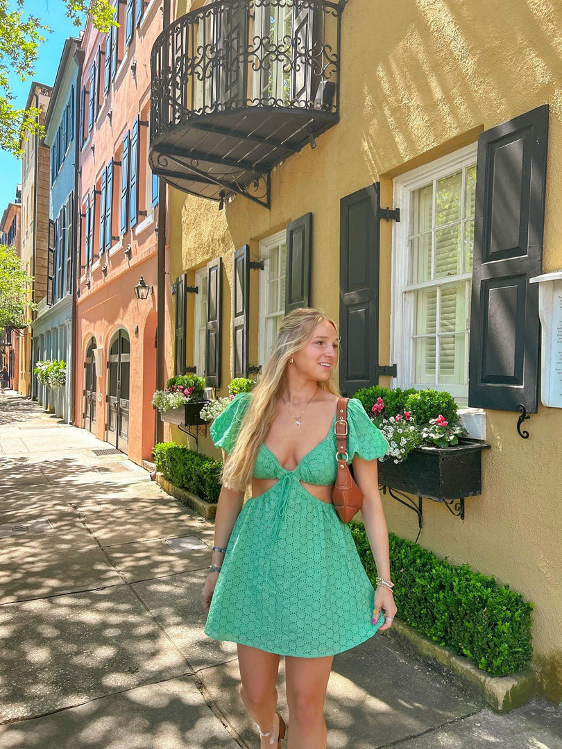 Influencer wearing green puff sleeve mini dress with V-neckline and waist cutout on historic city street.