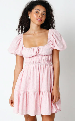 Woman wearing the Kendall pink eyelet puff sleeve mini dress with a smocked bodice and tiered babydoll skirt