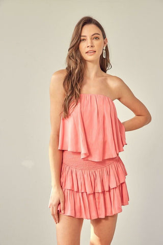 Model wearing the Monaco Coral Strapless Ruffle Romper, a tiered mini dress style romper for summer vacations.