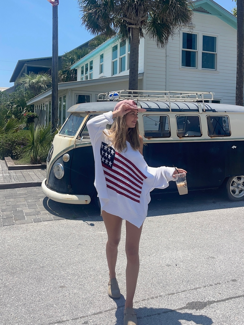 Women in the land of free white american flag sweater twirling around outdoors on a sunny day