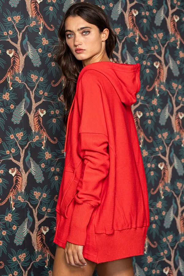 Woman wearing a red hoodie in front of a patterned wall with tigers and foliage.