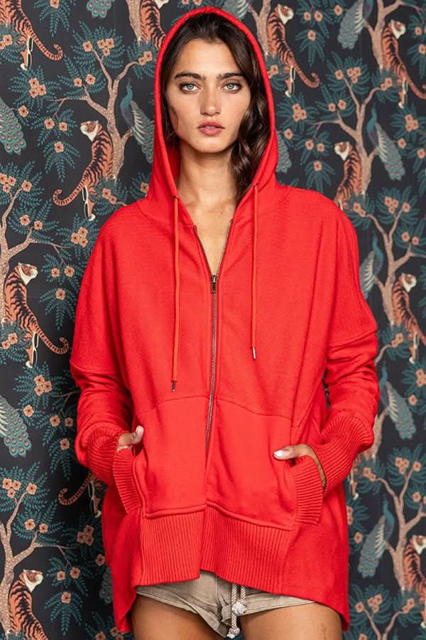 Person wearing a red hoodie against a patterned wall with tigers and floral designs.