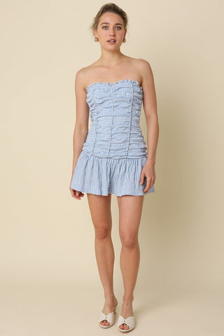 Model wearing Taryn Blue Gingham Strapless Mini Dress to showcase the flared mini skirt and fit