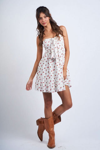 Model wearing a white and red floral babydoll mini dress with an empire waist and tie front