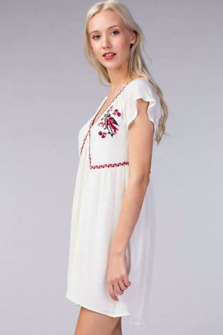 Side view of white gauze babydoll dress with embroidered trim and flowy skirt