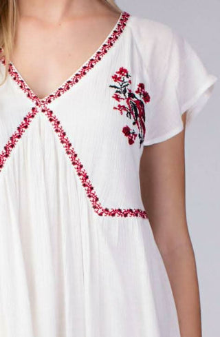 Close up of white babydoll dress with red embroidered trim and v neckline