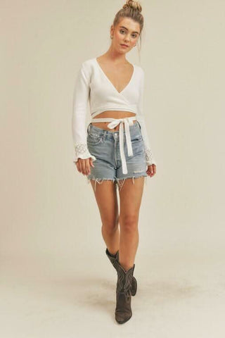 Model wearing a white wrap cropped sweater with shorts and cowgirl boots