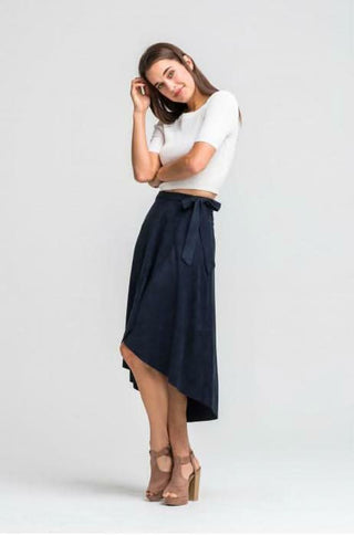 A model walking in a navy suede wrap skirt, showing the asymmetrical front slit and flowy movement.